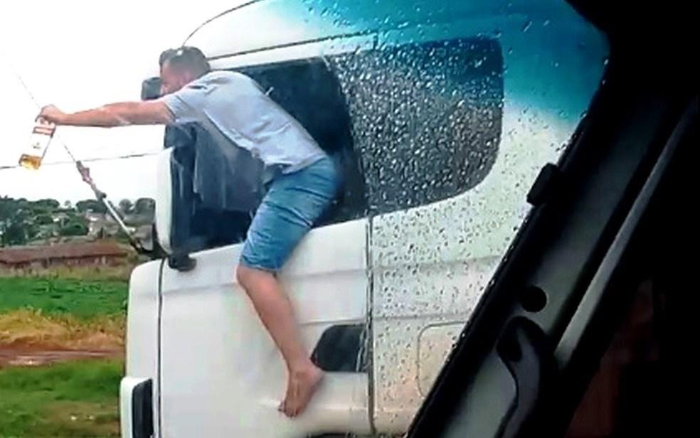 Caminhoneiro é filmado com corpo para fora de veículo com garrafa de bebida na mão enquanto dirige